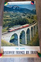 Photographic poster showing train crossing large stone viaduct in the Alps with mountainous background, promotional text for French National Railroads and travel by train