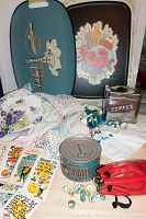 Overview of items showing two decorative trays, vintage textiles including doilies, aluminum coffee canister, unopened Maxwell House tin, Valentines cards, bag of marbles.