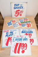 Eight hand-painted store sale signs from Honest Ed's with product names and prices, grouped by kitchen and electronics themes.