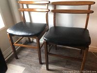 Pair of vintage midcentury wooden chairs with black vinyl seats, showing overall condition and style.