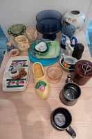 Overview of vintage dishes, glassware, and figurines arranged on a wooden table showing multiple items with different shapes and colors.