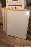 Three large wooden frames with light natural wood finish and anti-reflective glass panels, standing side by side.