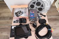 Full view of the lot including two digital cameras, NES games stack, Blackberry Playbook, film reel canister, charger, and RCA cables.