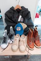 Full lot showing all items: grey Winnipeg Jets hooded jacket hanging on wall, blue and beige vintage Labatt's cap, two pairs of sneakers (white Converse high-tops and beige casual), and brown leather Doc Martens boots.