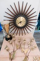 Full view of starburst clock with brass desk lamp and two-piece brass butterfly wall decor on table.