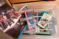 Overview of multiple items including event programs, metal clips, craft papers, and small stands inside plastic container