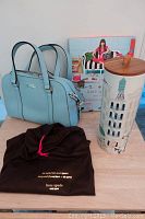Lot items including a light blue handbag, a cityscape decorative canister with wooden lid, and a coffee table book.