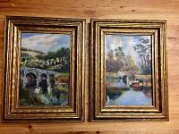 Photo showing both framed original oil paintings side by side on a wooden surface, highlighting frame condition and painting details