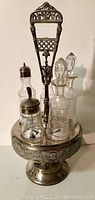 Full view of the antique cruet set showing the silver-plated stand holding four glass bottles with lids and stoppers.