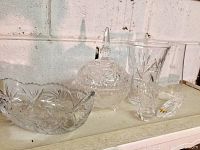 Six pieces of clear glassware arranged on a shelf showing the variety in the lot including the candy dish, serving bowl, glasses, and lid.