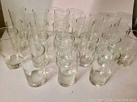 Overview image showing 21 clear vintage heavy glass drinking glasses arranged in rows.