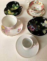 Five cups and saucers arranged on white surface with varying floral patterns, showing full tops and handles.