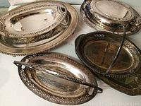 Six vintage silverplate pieces including oval trays with pierced edges, a round serving platter, and a covered dish with handle.