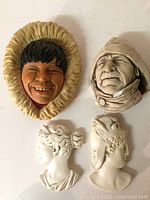 Four wall hanging faces displayed including one colored Bossons piece and three white plaster faces.