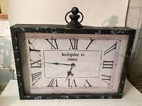 Rectangular reproduction Paris wall clock with black distressed frame and Roman numerals with cream colored clock face showing "Antiquite de Paris" text.