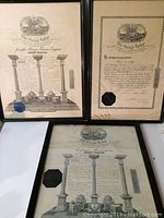 Three framed certificates from Grand Lodge Canada on flat white surface, two standing vertically, one horizontally.
