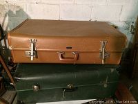 Side view of the two stacked vintage suitcases, showing the tan suitcase on top of the green suitcase, highlighting size and condition.