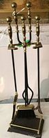 Full view of the fireplace tool set including stand, shovel, broom, poker, and tongs with brass and black iron materials.