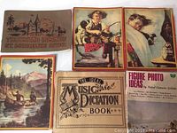 Group photo showing all books and notebooks laid out: Thousand Islands 1925 book, Ideal Music Dictation Book, Figure Photo Ideas photography book, and three illustrated blank softcover notebooks.
