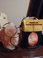 Photo of the salt crystal lamp with original box behind it. The lamp is pinkish in color with an attached power cord and switch visible.