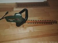 Bosch green electric hedge trimmer with long serrated blades placed on wooden floor