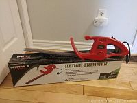 Red electric hedge trimmer placed on top of original box. Box shows product image and branding details.