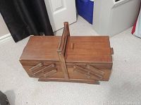 Closed antique wooden folding sewing box with handle on top.
