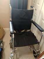 Front view of collapsible wheelchair showing black fabric seat and backrest, padded armrests and chrome frame