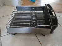 Photo of a stainless steel KitchenAid dish rack with two black plastic utensil holders on the right side, placed on tiled floor.