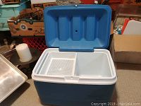Open view of the blue Rubbermaid cooler with white lid and ice grid interior