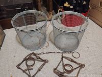 Two metal mesh minnow buckets and two rusted metal fishing traps arranged on carpeted floor.