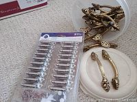 Photo showing the package of 20 satin nickel finish hinges and several bronze ornate cupboard pulls on carpet.