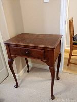 Closed vintage Singer sewing machine cabinet with single drawer and polished wooden finish, standing against a corner wall.