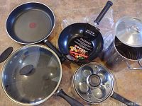 Non-stick frying pan, Paderno wok, glass lid, egg poacher insert, and tall metal pot with lid on floor.