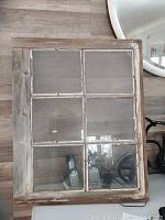 Close-up of old wood framed window decor showing six glass panes and weathered wood with chipped paint.
