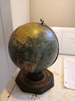 Photo shows an old metal globe measuring around 10x8 inches, mounted on a metal base with a ring support. Geographic details and country borders are visible on the globe's surface.