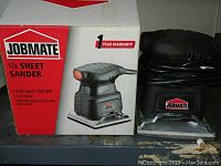 Jobmate 1/4 sheet sander sitting next to its original box showing key product features and branding.