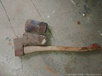 Photo showing one complete axe with wooden handle and two additional metal axe heads, all showing signs of wear and rust.