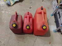 Photo of three red portable gas cans placed on the floor, two smaller 10 litre cans and one larger 20 litre can, all with yellow and black screw caps.