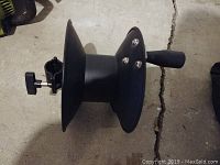Side view of black plastic hose reel showing spool and adjustable clamp attachment.
