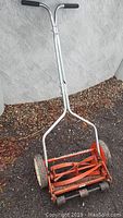 Full view of vintage manual push mower showing handle, wheels, and orange rotary blade section