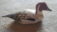 Side view of hand carved and painted wooden duck decoy resembling a male Northern Pintail duck with detailed patterns and colors