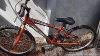 Side view of orange Sport MTB bike showing frame, black seat, and tires in sunlight.