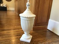 Front view of tall white glass vessel with removable lid attached.