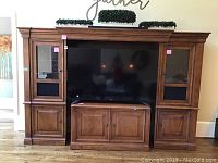 Front view of entertainment center assembled with a TV in the middle, showing left and right wooden cabinets with glass panes and lower cabinets.