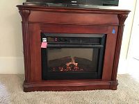 Front view of wooden mantel with electric fireplace insert, glowing logs visible.