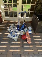 Photo showing pool basketball net, volleyball net, inflatable volleyball, small basketball, football, fish-themed cushions, wooden paddleboard, and pool toys on outdoor patio.