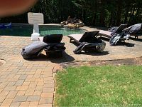 Two rattan chaise lounges positioned poolside on brick pavers, covers and cushions visible