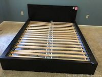 Full view of black metal and wood bed frame with wooden slats and matching headboard against a blue wall.