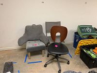 Four chairs and foot stool arranged side by side against wall: gray plush backrest chair, black office chair on casters with wooden back, gray folding chair and gray foot stool partially visible.